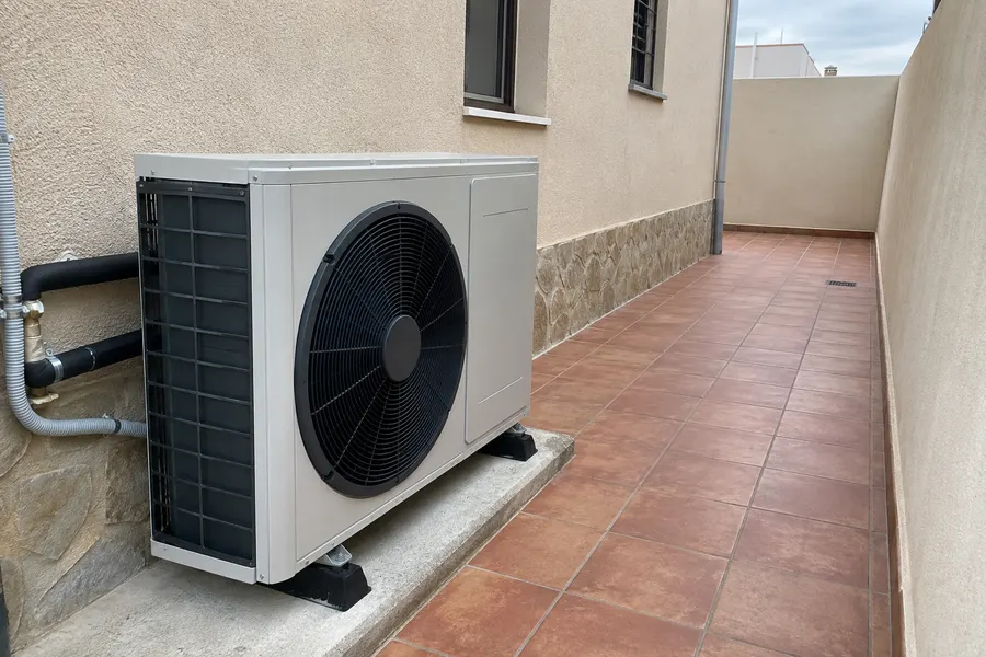 Aerotermia aire-agua Unidad exterior de aerotermia en un lateral de vivienda con pavimento de terracota